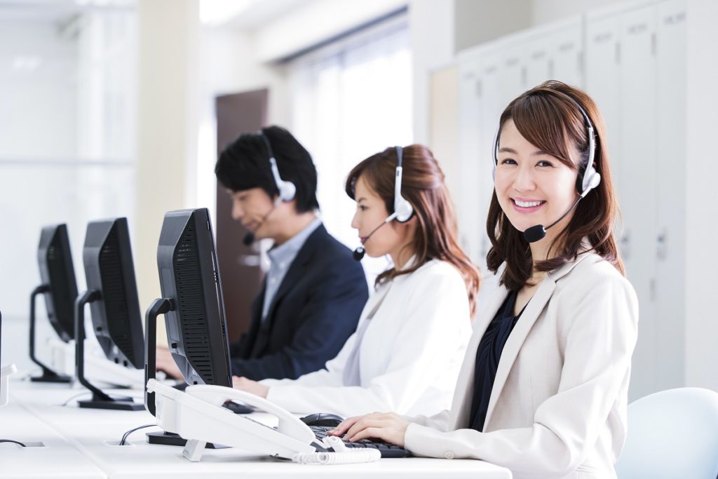 電話代行業者の受付を担当する30代の女性スタッフが、お客様からの電話に親身に対応している様子。女性スタッフは落ち着いた声で丁寧に挨拶し、「どのようなご用件でしょうか？」と優しく問いかけながら、お客様の話にしっかり耳を傾けています。依頼内容や希望する対応を一つひとつ確認し、「そのように承りました」「ご安心ください、責任を持って対応いたします」と安心感を与える言葉を添えて対応。表情は柔らかく、電話越しでも誠実さや親しみやすさが伝わるような雰囲気で、信頼できるパートナーとしてお客様に寄り添っている様子が感じられます。